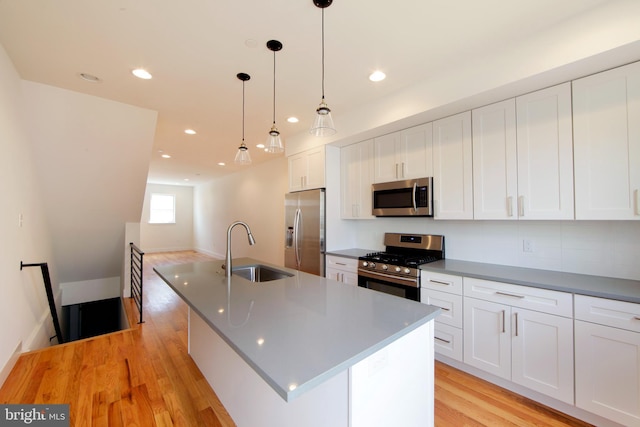 kitchen featuring a kitchen island with sink, stainless steel appliances, decorative light fixtures, sink, and white cabinets