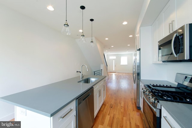 kitchen with stainless steel appliances, white cabinets, decorative light fixtures, sink, and a kitchen island with sink