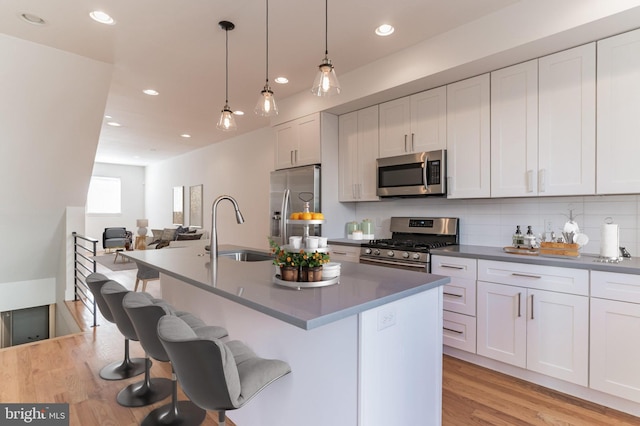 kitchen with a kitchen bar, sink, appliances with stainless steel finishes, white cabinetry, and decorative light fixtures