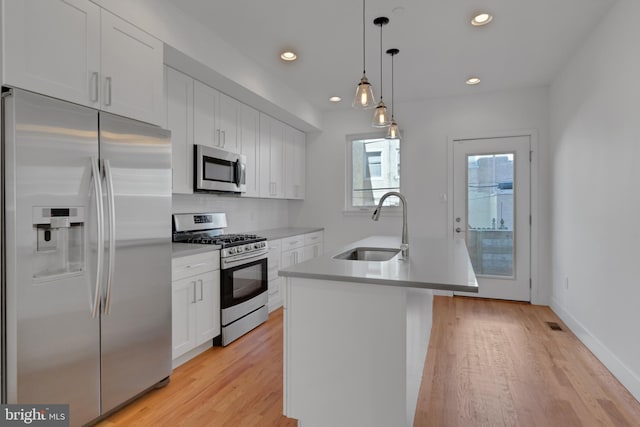 kitchen with white cabinetry, a center island with sink, stainless steel appliances, decorative light fixtures, and sink