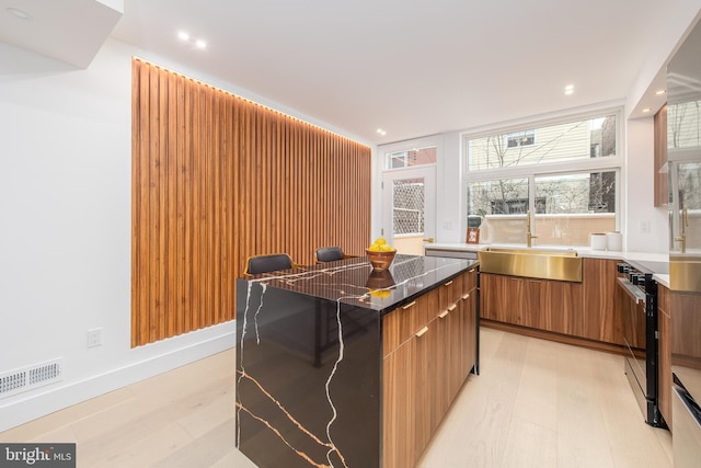 kitchen with brown cabinetry, modern cabinets, a breakfast bar, a center island, and a sink