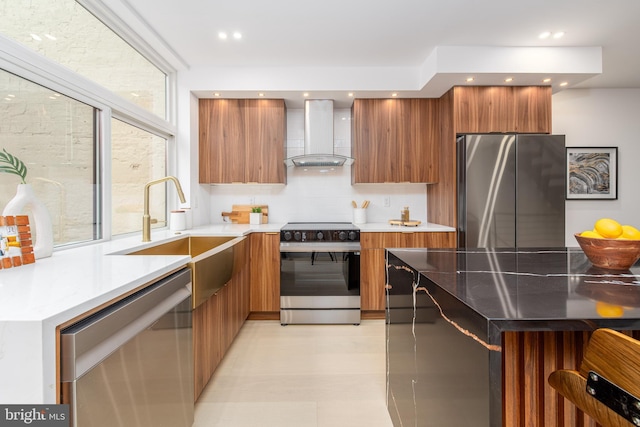 kitchen with appliances with stainless steel finishes, brown cabinetry, a sink, wall chimney range hood, and modern cabinets