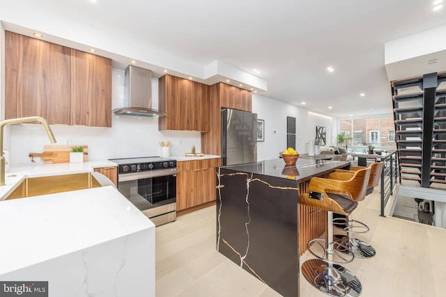 kitchen featuring brown cabinetry, wall chimney exhaust hood, modern cabinets, and stainless steel appliances