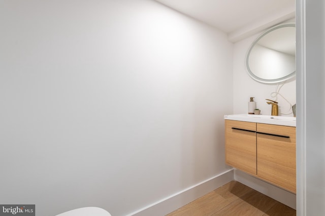 half bath with baseboards, wood finished floors, and vanity