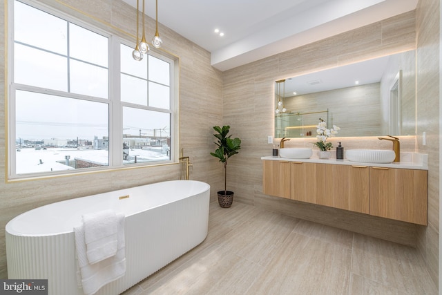 full bathroom with double vanity, a freestanding tub, tile walls, and a sink