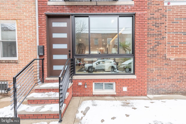 snow covered property entrance featuring brick siding