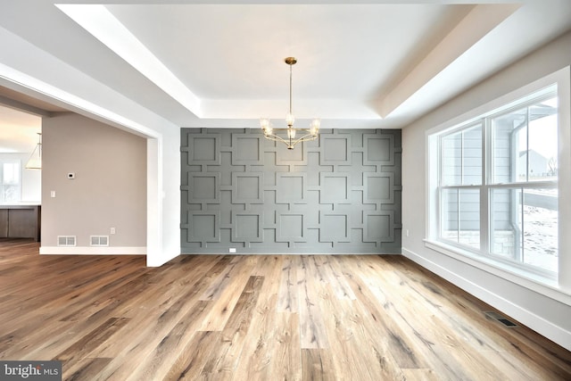 unfurnished dining area with hardwood / wood-style floors, a notable chandelier, and a raised ceiling