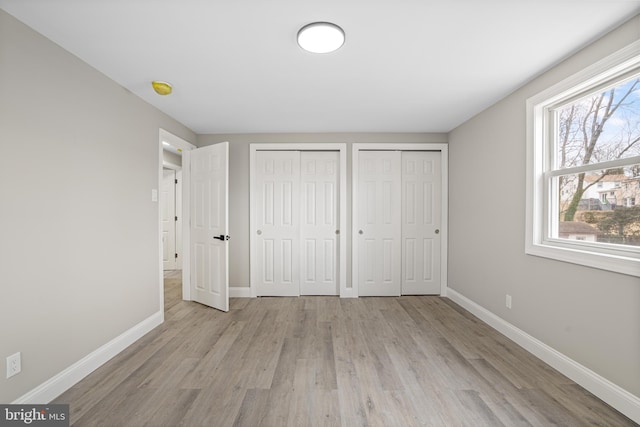 unfurnished bedroom with light wood-style flooring, baseboards, and multiple closets