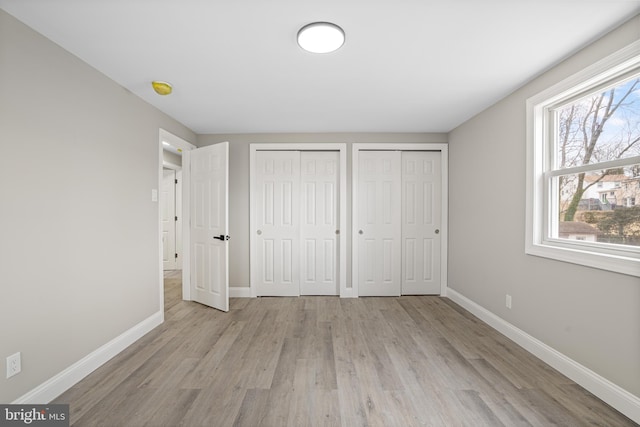 unfurnished bedroom featuring baseboards, light wood-style flooring, and multiple closets