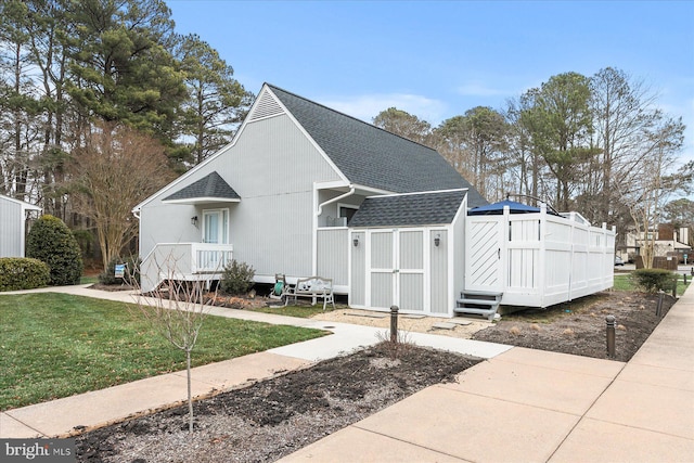 view of front of house with a storage unit, a shingled roof, an outbuilding, and a front yard