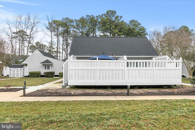 view of front of property featuring a shed, roof with shingles, and a front yard