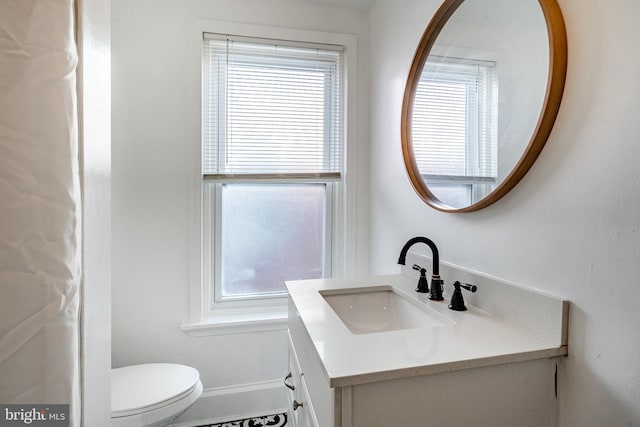 half bath with toilet, baseboards, and vanity