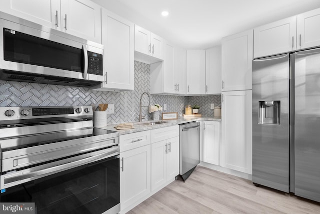 kitchen with appliances with stainless steel finishes, white cabinets, decorative backsplash, a sink, and light wood-type flooring
