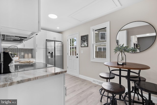 kitchen with stainless steel refrigerator with ice dispenser, light wood-type flooring, white cabinetry, light stone countertops, and baseboards