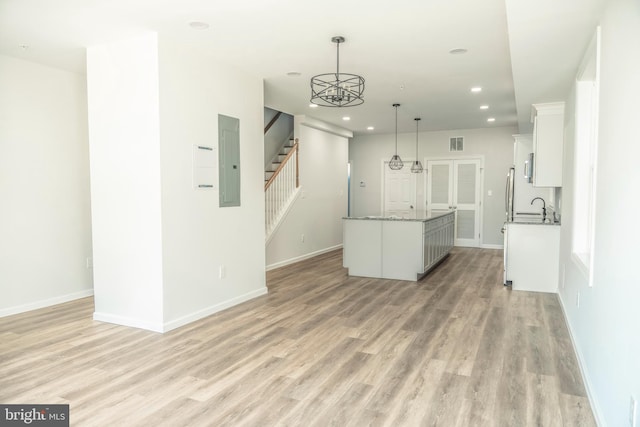 kitchen with a sink, light wood-style floors, white cabinets, hanging light fixtures, and electric panel