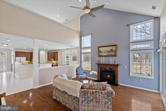 living room with visible vents, a fireplace with flush hearth, wood finished floors, baseboards, and ceiling fan