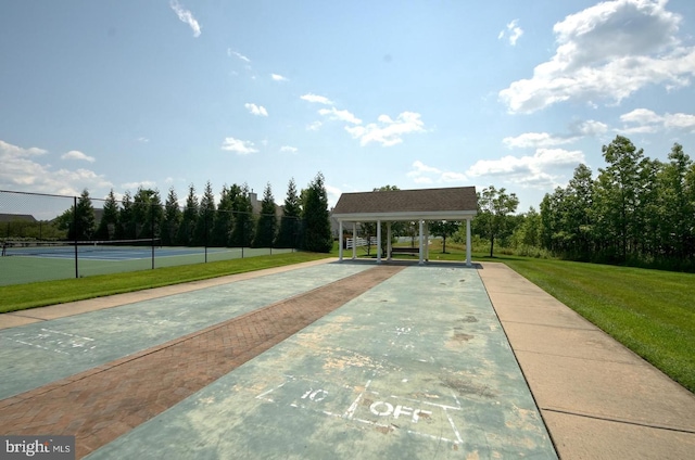 view of home's community with a yard, a tennis court, and fence