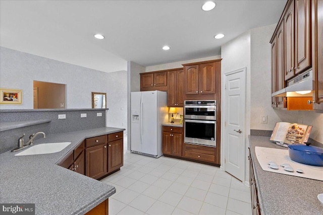 kitchen featuring recessed lighting, a sink, under cabinet range hood, white fridge with ice dispenser, and double oven