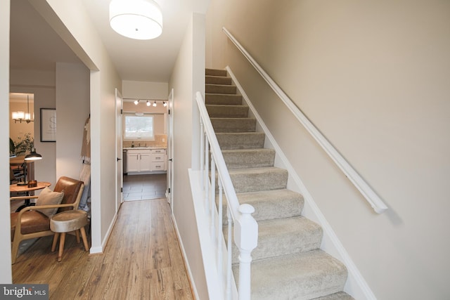 stairs featuring sink, a notable chandelier, and wood-type flooring