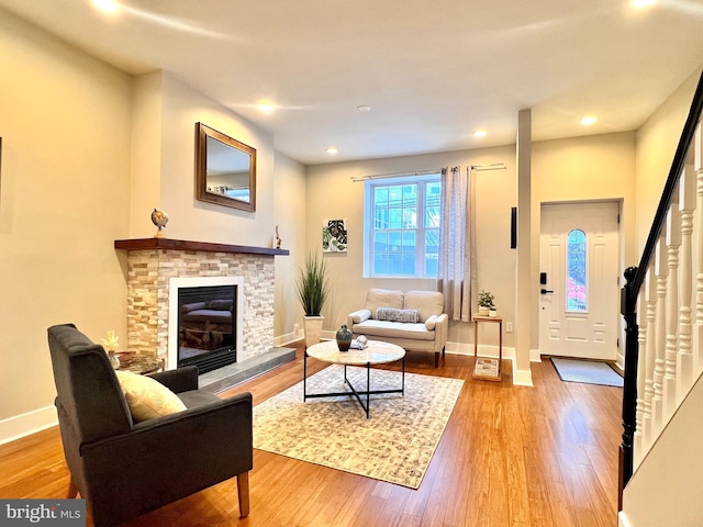 living area featuring recessed lighting, a stone fireplace, wood finished floors, baseboards, and stairs