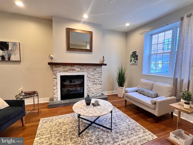 living area with a stone fireplace, dark wood-type flooring, recessed lighting, and baseboards