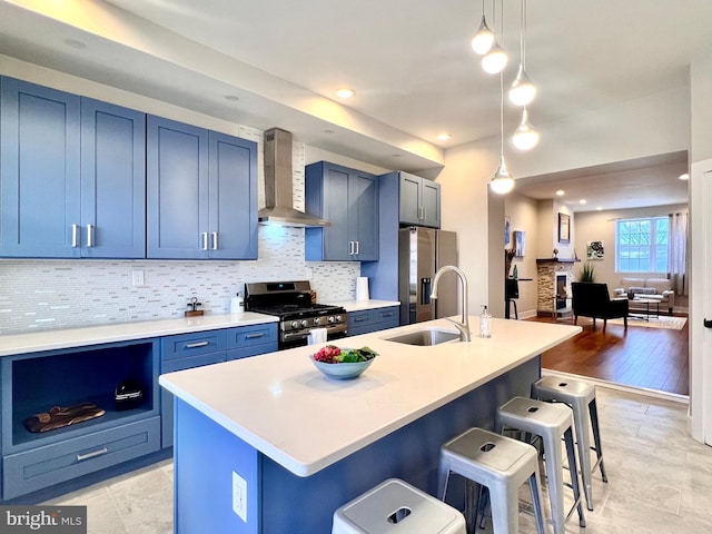 kitchen featuring an island with sink, hanging light fixtures, stainless steel appliances, a breakfast bar area, and wall chimney exhaust hood