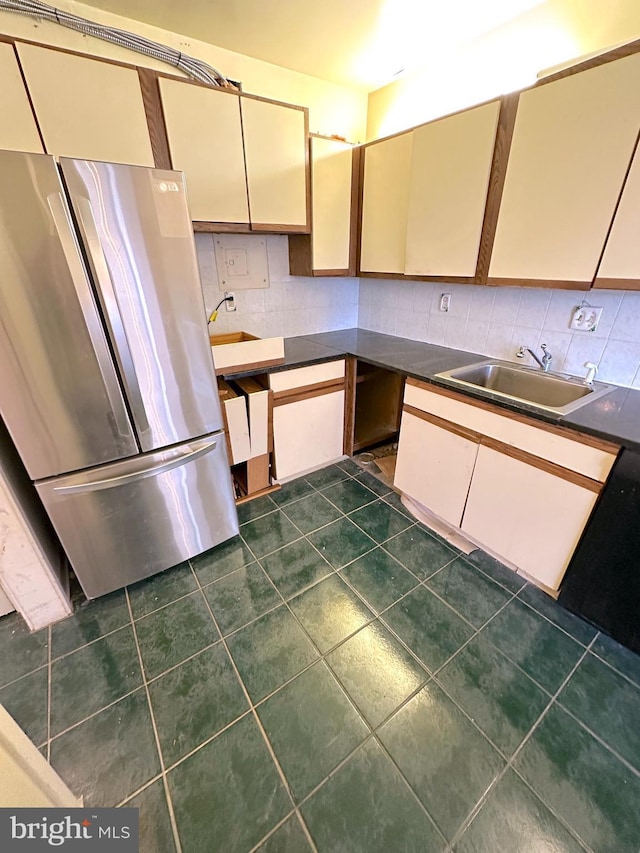 kitchen with cream cabinets, stainless steel refrigerator, sink, backsplash, and dark tile patterned flooring