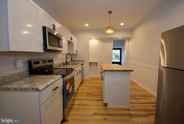 kitchen with wooden counters, stainless steel appliances, pendant lighting, sink, and white cabinetry