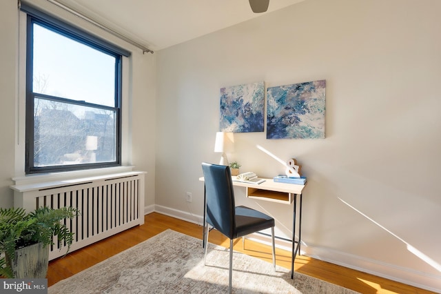 office area with radiator heating unit, baseboards, and wood finished floors