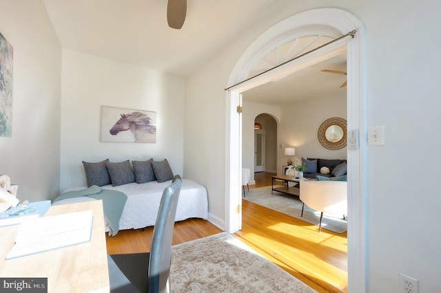 bedroom with arched walkways, ceiling fan, wood finished floors, and baseboards