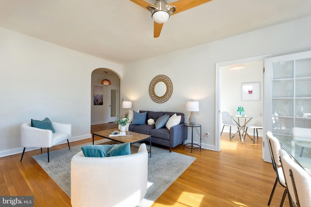 living area with light wood-style floors, baseboards, arched walkways, and a ceiling fan