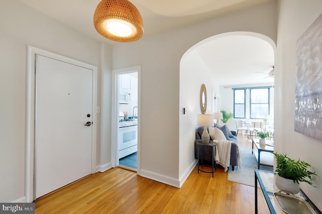 foyer entrance featuring arched walkways, light wood finished floors, and baseboards