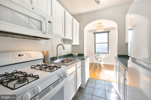 kitchen featuring white appliances, white cabinets, dark countertops, dark tile patterned floors, and a sink