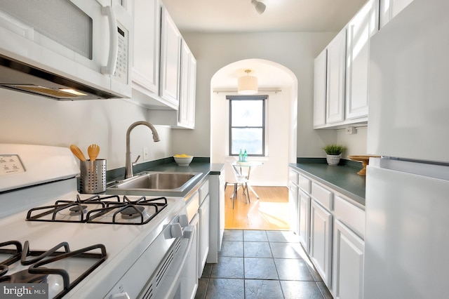 kitchen featuring white appliances, white cabinetry, arched walkways, and a sink