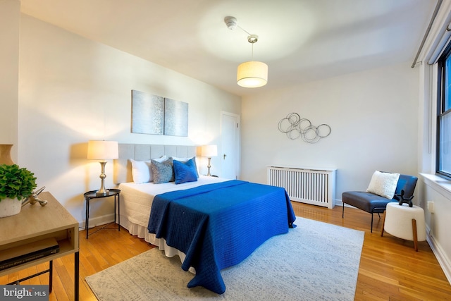 bedroom with radiator, light wood-type flooring, and baseboards