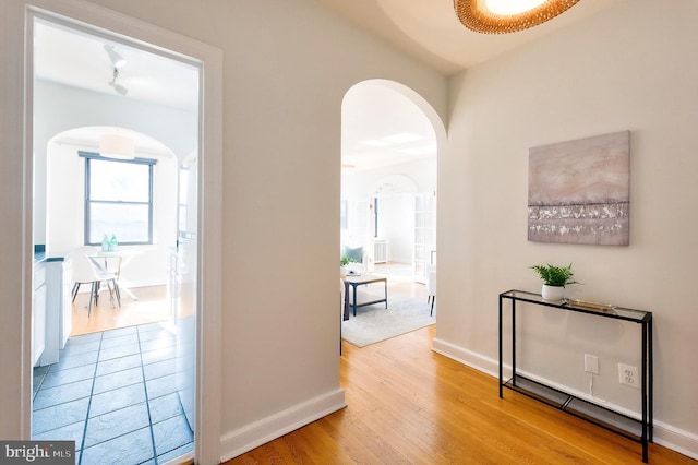 hallway with arched walkways, baseboards, and wood finished floors