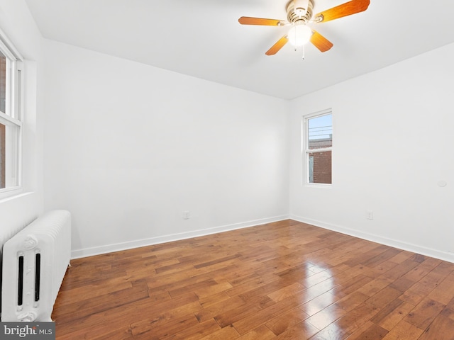 spare room featuring baseboards, ceiling fan, radiator heating unit, and hardwood / wood-style flooring