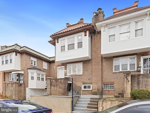 view of front of house featuring a tile roof, central AC, brick siding, and a chimney