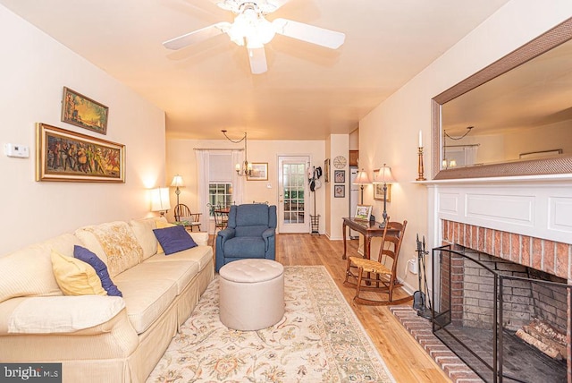 living room featuring ceiling fan with notable chandelier, light wood-type flooring, and a brick fireplace