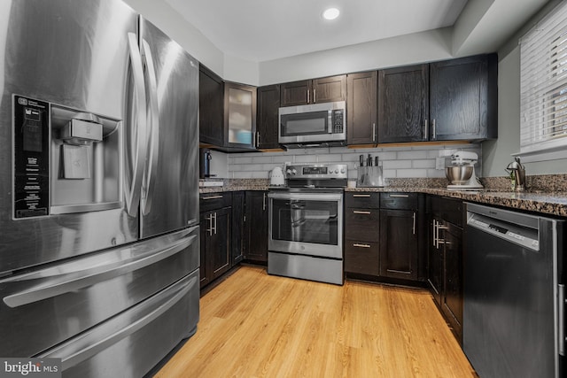 kitchen with appliances with stainless steel finishes, light wood-type flooring, dark stone counters, and tasteful backsplash