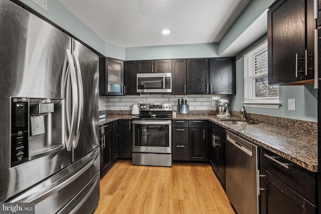 kitchen with stainless steel appliances, tasteful backsplash, a sink, and light wood-style floors