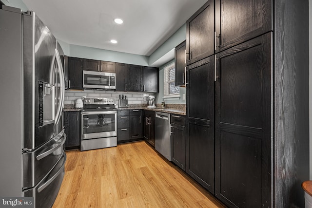 kitchen featuring recessed lighting, stainless steel appliances, light wood-style floors, backsplash, and dark stone countertops