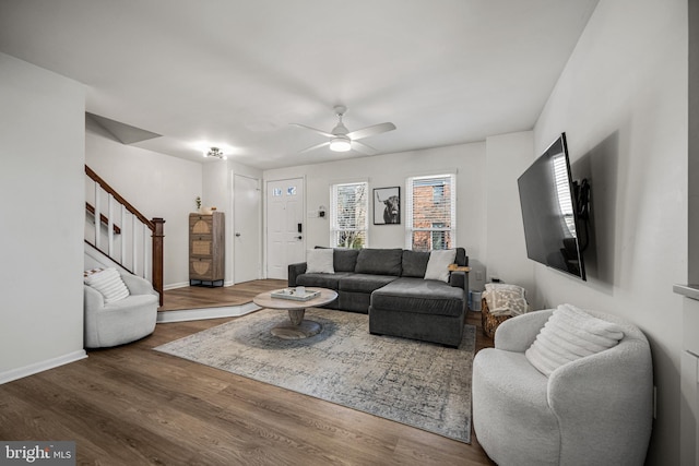 living area with baseboards, ceiling fan, stairway, and wood finished floors