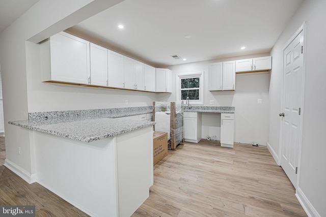 kitchen with light hardwood / wood-style floors, white cabinetry, light stone counters, and kitchen peninsula