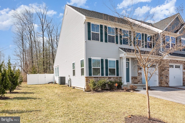 view of front of house with driveway, central AC unit, stone siding, fence, and a front yard