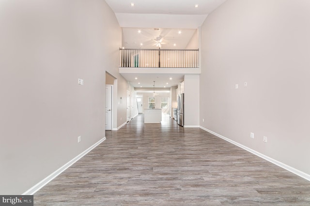 unfurnished living room featuring baseboards, a ceiling fan, wood finished floors, a high ceiling, and recessed lighting