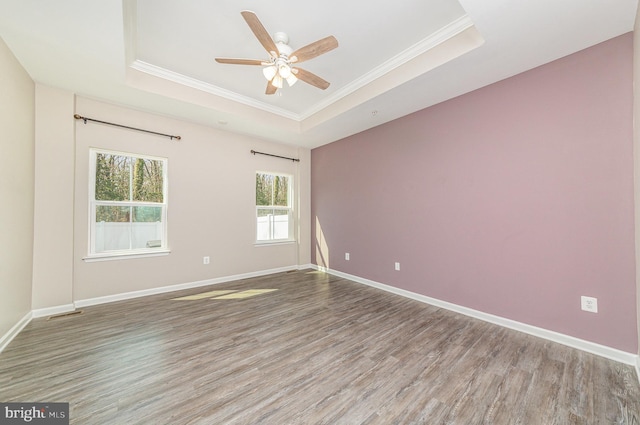 empty room with wood finished floors, a ceiling fan, baseboards, a tray ceiling, and crown molding