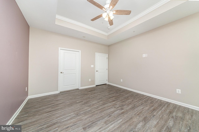 empty room with a raised ceiling, crown molding, baseboards, and wood finished floors