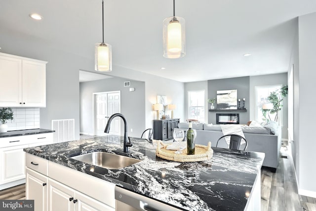 kitchen featuring dark wood-type flooring, an island with sink, dark stone counters, sink, and white cabinetry