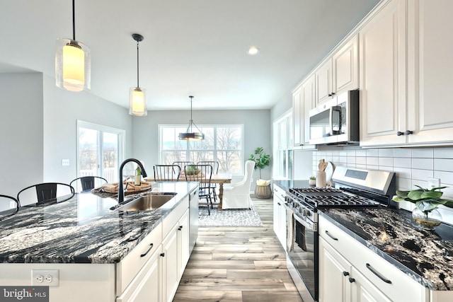 kitchen with appliances with stainless steel finishes, sink, white cabinetry, pendant lighting, and an island with sink